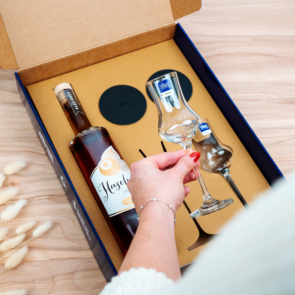 Geschenkbox Penninger - Blaue Verpackung mit zwei Magnet-Kristallgläsern Likör, einer Flasche Penninger Haselnuss und runden Metall-Nano-Gel-Pads in schwarz