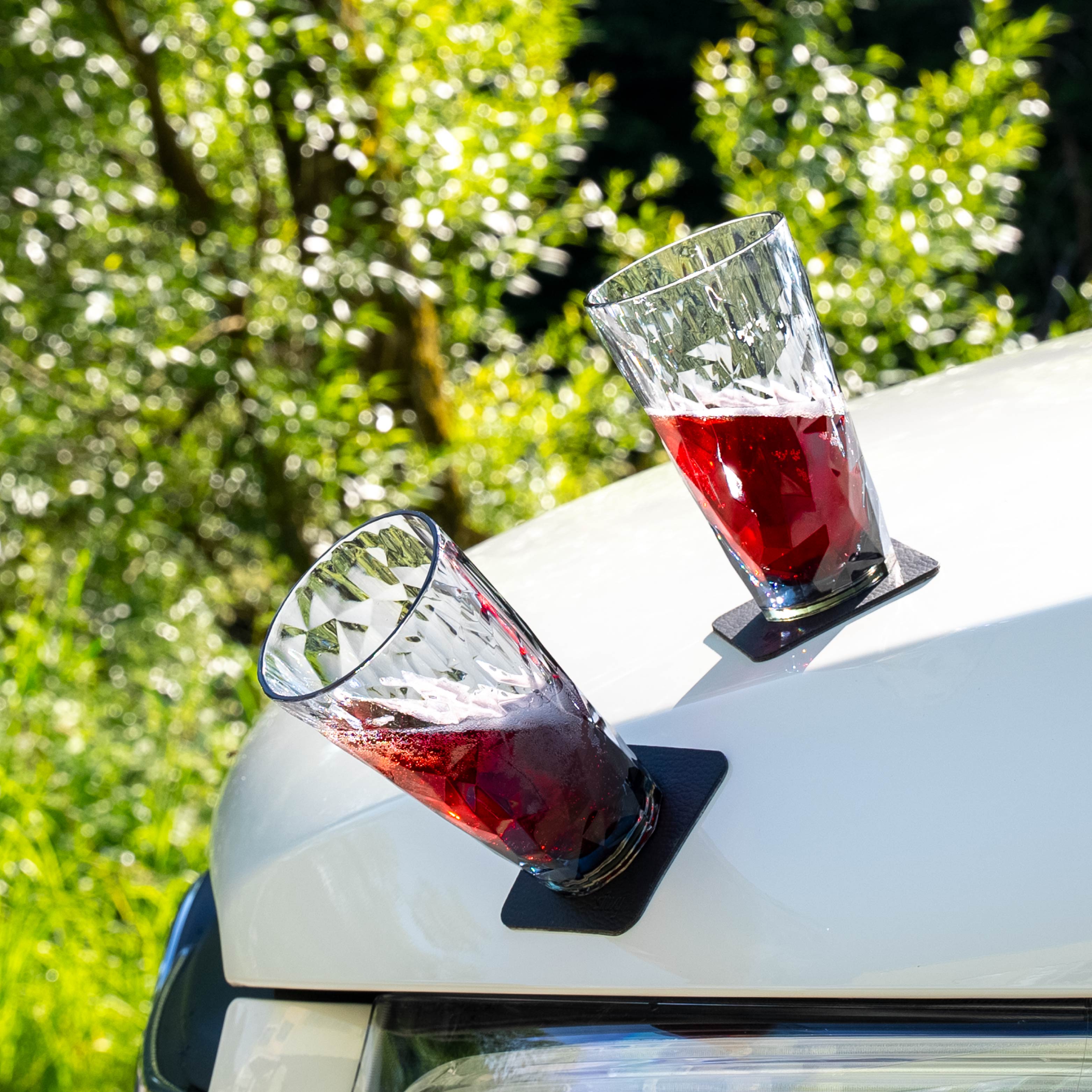 Zwei magnetische Kunststoffgläser Longdrink auf metallischer Motorhaube abgestellt 