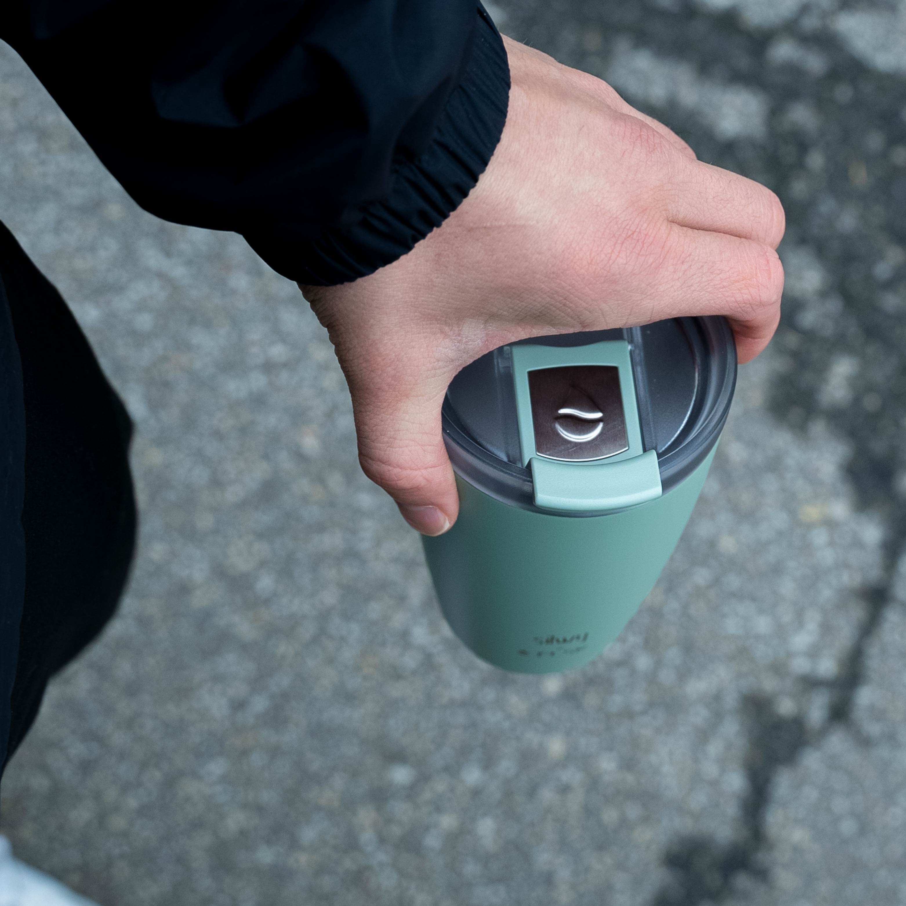 Der silwy x FLSK Thermocup in der Farbe sage, mit geschlossenem Deckel wird von oben gehalten 